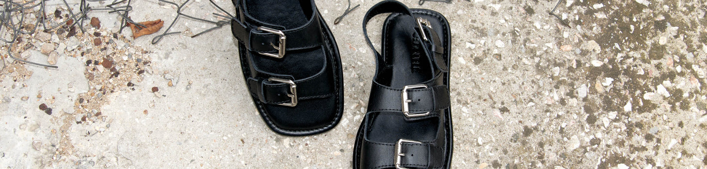 Ein Paar schwarze unisex Lederclogs auf Betonboden