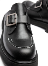 Lade das Bild in den Galerie-Viewer, Schuhspitze eines schwarzen, modischen Leder-Clogs. Zu sehen sind die abgerundete Karree-Form und ein Teil der leichten EVA-Sohle. Über dem Spann verläuft eine Monk-Schnalle in der Farbe Silber. Modisches Highlight ist zudem die weiße Naht, die auf der Schuhspitze verläuft.