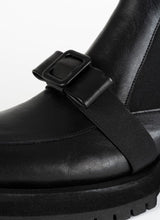 Lade das Bild in den Galerie-Viewer, Detailfoto eines schwarzen Chelseaboots aus Leder von CEDOUBLÉ mit dekorativer Schnalle in Schleifenoptik, die sich mit einem elastischen Band über den Spann schmiegt.