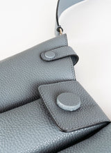 Lade das Bild in den Galerie-Viewer, Detailfoto einer Crossbody-Bag aus grauem, genarbtem Leder mit drei voneinander abgetrennten Fächern und einem farblich passenden, breiten Gurt aus Leder mit Karabinerhaken. Diese Handtasche ist genderfluid, angefertigt wurde sie von dem Newcomer-Label Cedoublé.