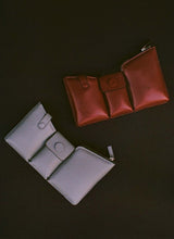 Lade das Bild in den Galerie-Viewer, Two bags on a black background, one is made out of puffy, dark red leather, the other is made out of grey pebbled leather. The bags have three compartments.