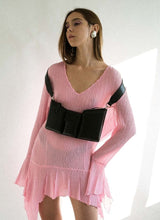 Lade das Bild in den Galerie-Viewer, Foto eines weiblichen Models mit langen braunen Haaren. Sie trägt ein leicht transparentes, hell pinkfarbenes Kleid mit gezackten Säumen, eine schwarze Handtasche aus Leder ist künstlerisch um beide Schultern gehängt, der Taschenkörper zeigt nach vorne und baumelt etwa auf Unterbrusthöhe der Frau. Das Model hat ihren Blick zur Seite gerichtet, sie steht vor einem weißen Hintergrund. Die Tasche ist von der Marke Cedoublé.