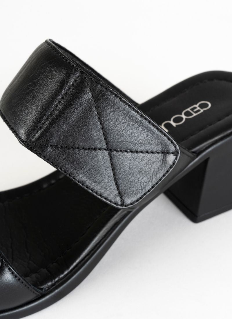 Detailfoto einer eleganten, aber alltagstauglichen Sandale in schwarzem Glattleder mit dekorativen Nähten an den Enden zweier gepolsterter Riemen.