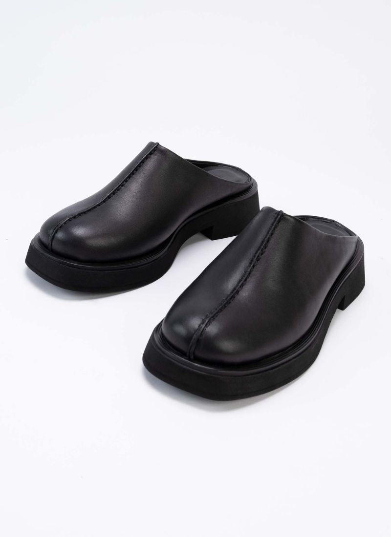 Exklusive Leder-Clogs mit geschlossener Front und offener Hinterkappe aus schwarzem Leder. Optisches Highlight ist die prägnante Mittelnaht, die vertikal über den Schaft verläuft. Die Mules sind hautfreundlich mit schwarzem Leder gefüttert und sorgen so allzeit für ein frisches Fußklima. Die Laufsohle ist leicht erhöht und ebenfalls schwarz.