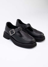 Load image into Gallery viewer, Foto eines Paares chunky Mary Jane Schuhe aus hochwertigem, schwarzem Leder. Die Schuhe sind mit schwarzem Leder gefüttert, die Laufsohle mit dezentem Plateau ist schwarz, die Schnalle eckig und silber. Typisch für diesen Schuhstyle gibt es seitlich auf dem Schaft verlaufende Aussparungen, die den Blick auf einen Teil des Fußes freilegen.
