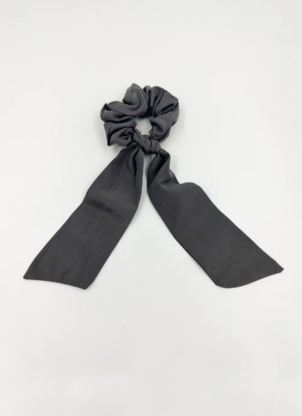 Haargummi mit dunkelgrauem Seidenbezug und einem daran geknoteten, schmalen Seidentuch. Beide Teile können auch separat voneinander getragen werden.