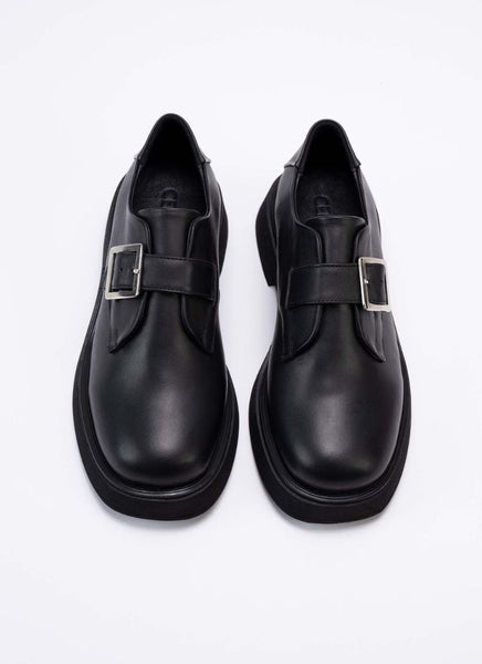 Draufsicht eines Paares Unisex-Halbschuhe aus dem Hause Cedoublé. Die Schuhe sind aus Qualitätsleder in schwarz gefertigt. Dieses Leder ist mit dem Gold-Standard der Leather Working Group ausgezeichnet und weist neben angenehmen Trageeigenschaften auch einen feinen Glanz auf. Über dem Spann des Schuhs befindet sich ein Lederriemen mit einer eckigen, silberfarbenen Schnalle. Die Front der Schuhe ist eckig und leicht abgerundet. Es handelt sich um einen modischen Klassiker.
