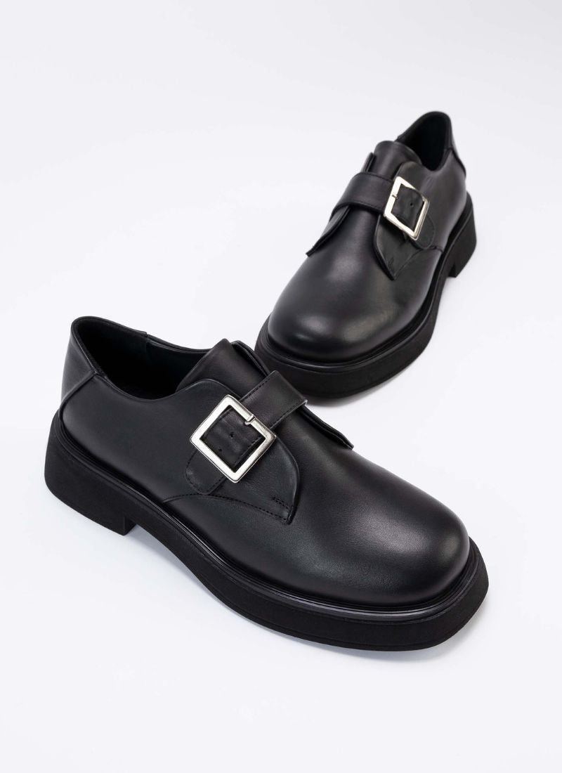 Ein Paar luxuriöse Halbschuhe aus hochwertigem, schwarzem Leder mit Lederriemen über dem Spann und silberfarbener, eckiger Schnalle. Auch die Sohle und das Futter sind passend schwarz. Die Schuhe sind vom Hersteller Cedoublé und werden unter fairen Bedingungen in Europa produziert.