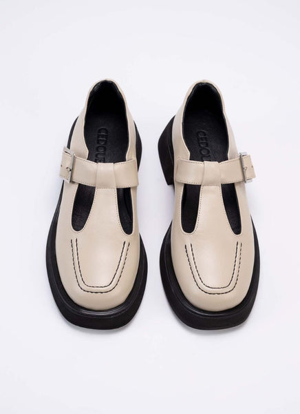 Produktfoto von einem Paar Lederschuhe im Mary Jane Stil in hellem Cremeton mit subtilem Schimmer. Die Sohle, das Futter und die Ziernähte auf der Schuhfront sind schwarz.