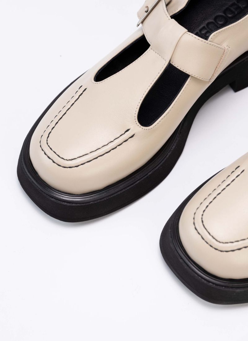 Detailfoto eines cremefarbenen Mary Jane Schuhs aus Echtleder. Als Kontrast wurden schwarzes Lederfutter, eine schwarze Laufsohle und schwarzes Lederfutter verwendet. Die Schuhfront wird von einer Wulstnaht mit schwarzem Stitching geziert.