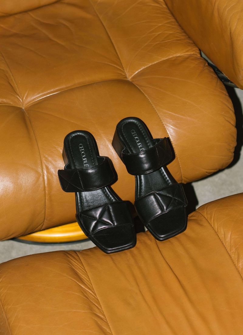 Elegant-alltagstaugliche Absatzsandale aus schwarzem Leder mit Karreefront auf einem cognacfarbenen Ledersessel