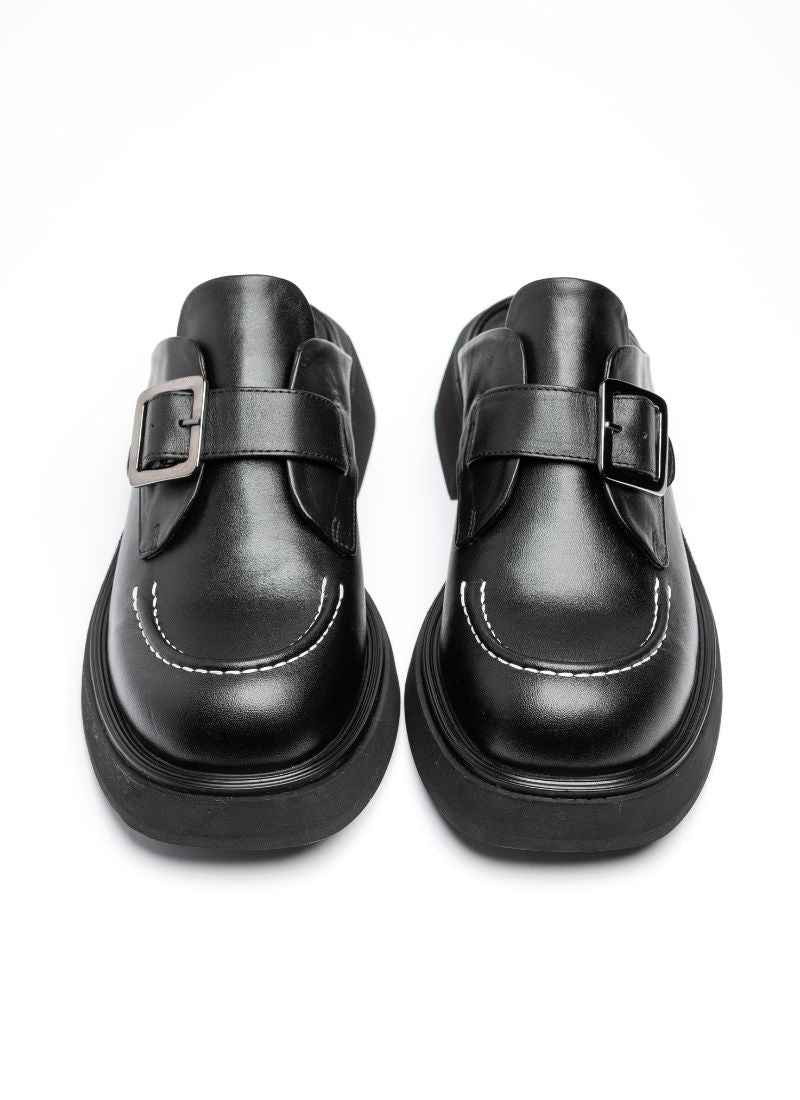 Zwei parallel zueinender stehende Clogs aus schwarzem Leder. Im Fokus stehen die abgerundete Karreeform sowie die weiße Kontrastnaht auf der Schuhspitze.