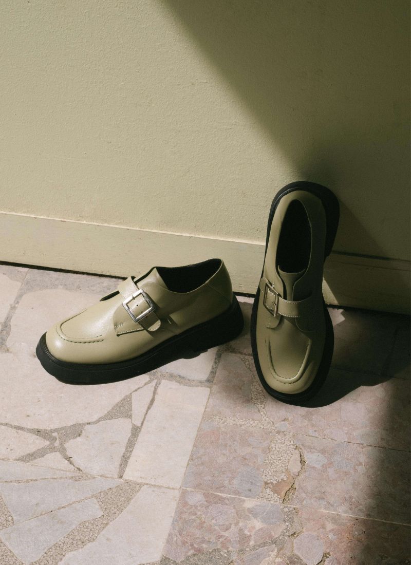 Ein Paar grüner unisex Monks steht vor einer farblich passenden, salbeigrünen Wand 