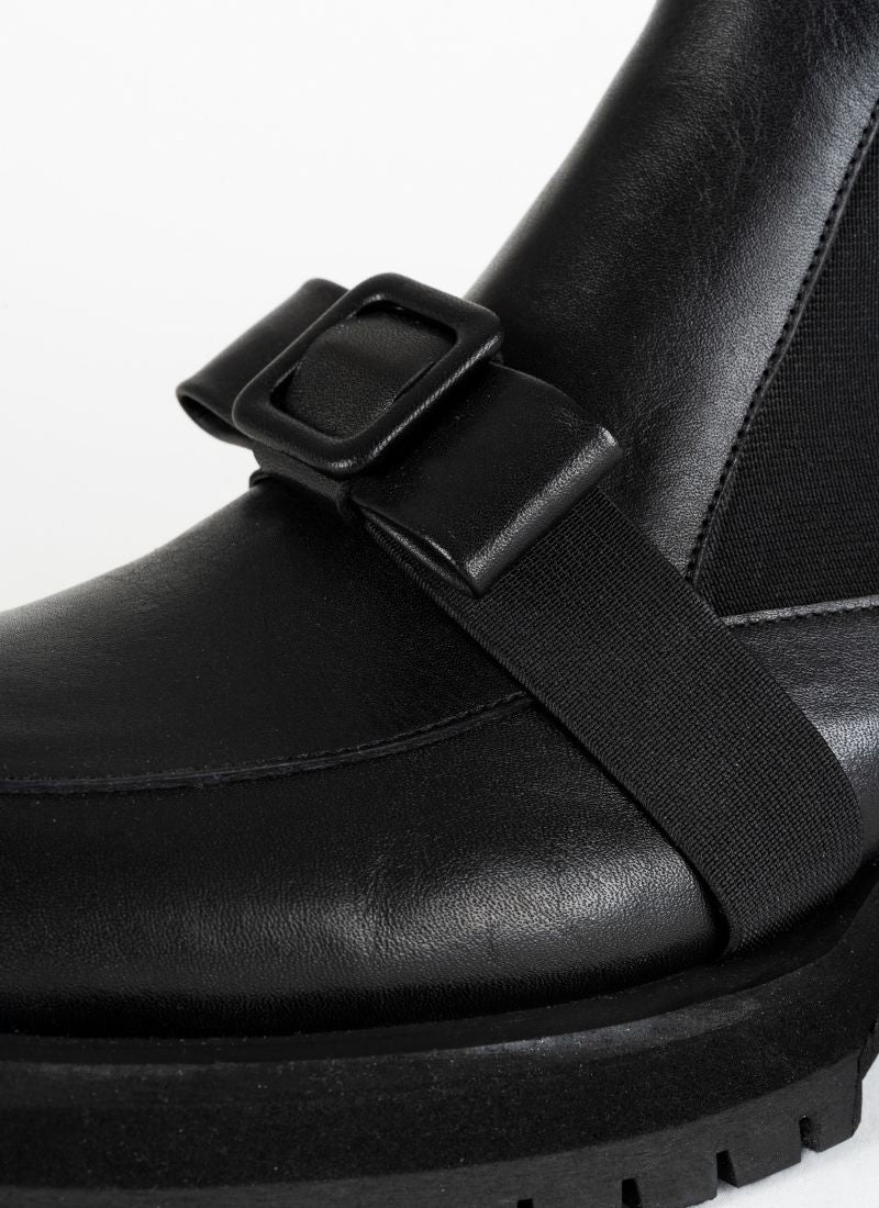 Detailfoto eines schwarzen Chelseaboots aus Leder von CEDOUBLÉ mit dekorativer Schnalle in Schleifenoptik, die sich mit einem elastischen Band über den Spann schmiegt.