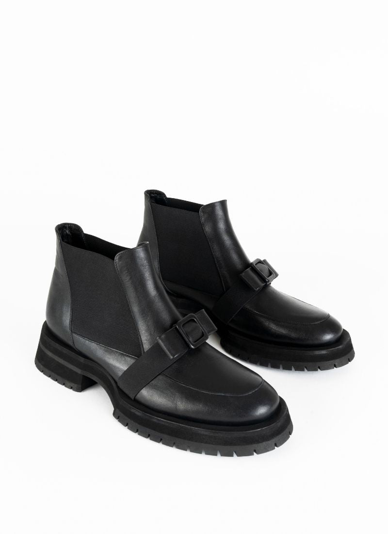 Ein Paar schwarze Chelseaboots aus Leder mit weitflächigem Elastikeinsatz und dekorativer Schnalle in Schleifenoptik. Dieses Schleifendetail schmiegt sich über den Spann.
