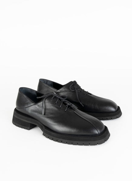 Produktfoto eines schwarzen Derbys aus Leder mit Oxford-Schnürung und ausgeprägter Laufsohle. Eine asymmetrische Naht ziert die Schuhfront