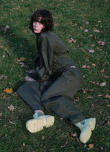 Load image into Gallery viewer, Bild eines weiblichen Models, welches auf einer herbstlichen Grasfläche liegt. Ihre Hände sind aufgestützt, die fokussiert die Kamera. Bekleidet ist die junge Frau mit einem khakifarbenen Zweiteiler bestehend aus Hose und Jacke. An den Füßen trägt sie hellgrüne Leder Lug Boots aus dem Hause Cedoublé, welches ein angesagtes Online-Schuhlabel aus Deutschland ist. Die Schuhe erinnern an Modelle von Bottega Veneta oder Ganni.
