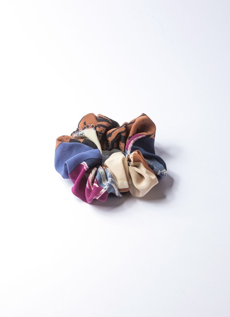 Bild eines Scrunchies aus 100% upcycled Seide. Dieses Accessoire wurde lokal in Deutschland per Hand unter fairen Bedingungen hergestellt und ist nachhaltig. Die Farbgebung beinhaltet creme, lila, blau, schwarz und braun. Hersteller ist das Schuh-Label CEDOUBLÉ.
