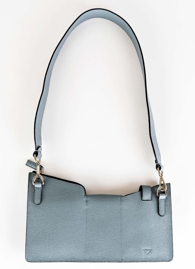 Rückansicht einer Crossbody Tasche aus grauem Leder. Diese Tasche ist von der Marke Cedoublé. Sie verfügt über drei Taschenabteile, welche entweder mit Druckknopf oder Reißverschluss geschlossen werden können. Der Taschenhenkel kann mittels Karabinerhaken ausgetauscht oder abgenommen werden. Das Leder ist ein hochwertiges Kalbsleder, das Futter ist ein Lammleder. Der Taschenkörper ist leicht gefüttert. Insgesamt eine sehr praktische Tasche für viele Anlässe.