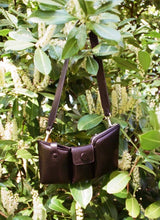 Load image into Gallery viewer, Puffy black leather bag by CEDOUBLÉ hanging in a bush with white blossoms on a sunny day 
